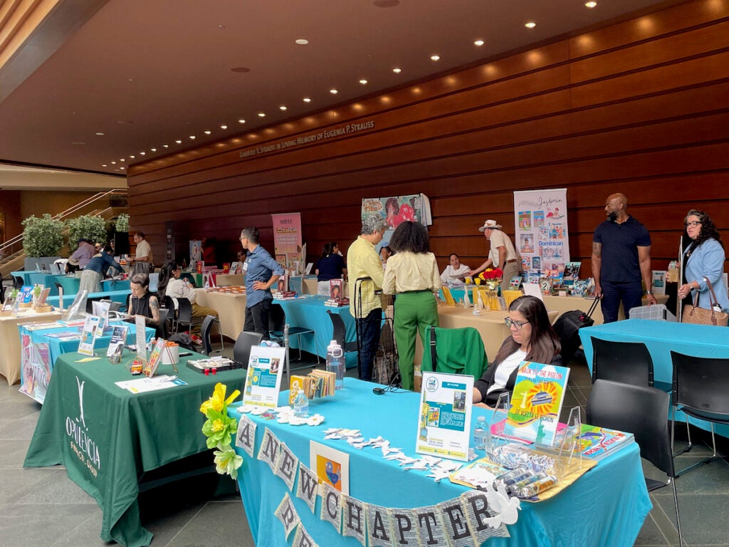 People sit behind tables with books displayed at a book fair