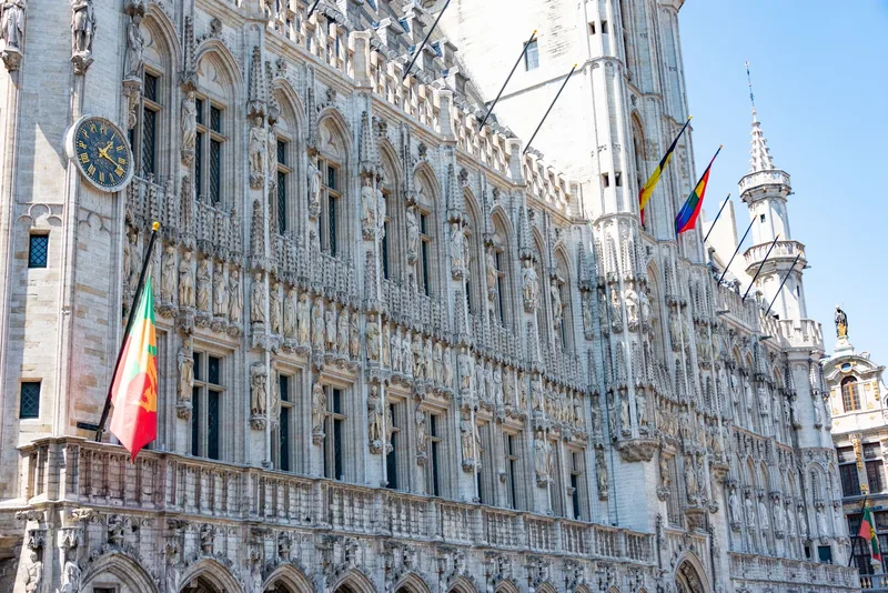 A detailed view of the Gothic-style Town Hall in Brussels with flags and intricate stonework. (stock photo via Pexels)