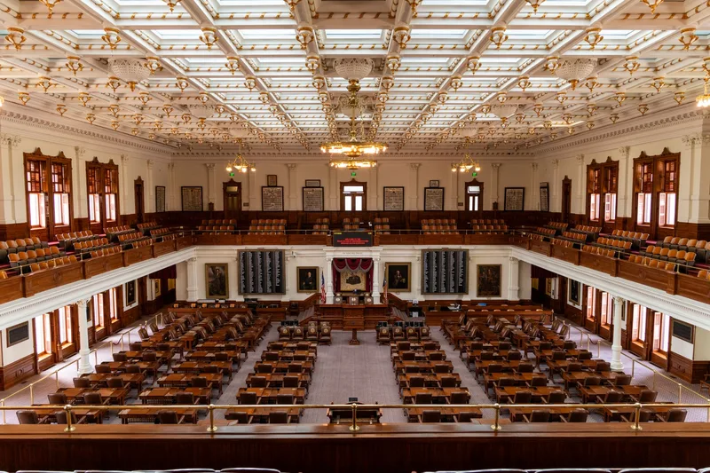Spacious interior of the Texas State Capitol House Chamber with seating and elaborate ceiling. (stock photo via Pexels)