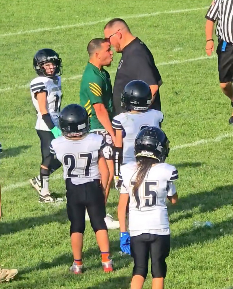 Two youth football coaches in a heated confrontation on a football field.