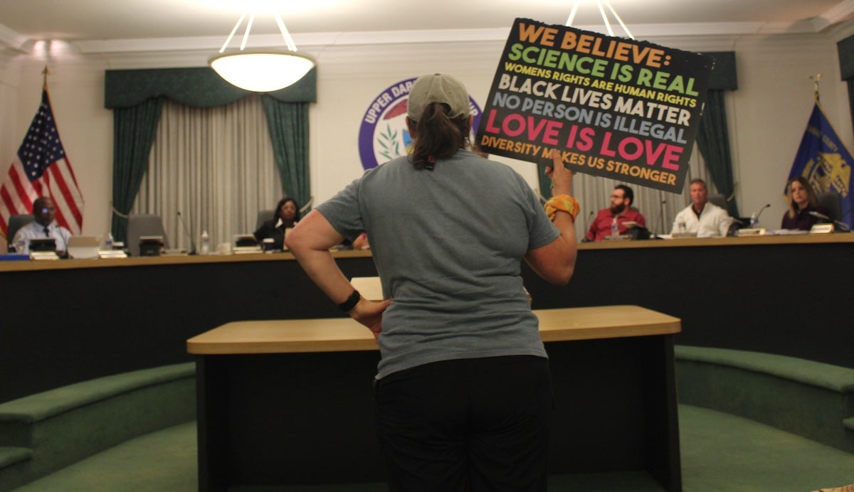A community member holds up a sign before Upper Darby Township Council that reads, ''We believe: science is real, women's rights are human rights, Black lives matter, no person is illegal, love is love, diversity makes us stronger''