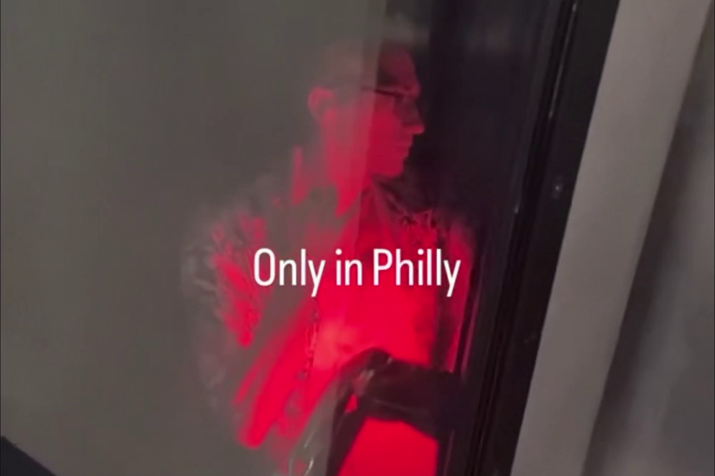 A man seen through a window, illuminated by red light, with the text "Only in Philly" superimposed on the image.