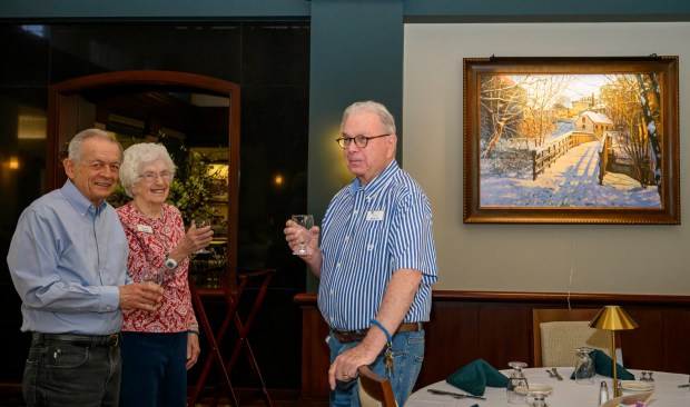 Kirkland Village Art Commission members Margie Mosher, Charles Lyman and Ned Bowne stand near a painting of Bethlehem's 1754 Waterworks by Sergei Yaralov, one of four recently installed in the main dining room of Kirkland Village, on Friday, Oct. 2, 2026, in Bethlehem. Residents donated money to purchase the art, part of a collection of over 800 pieces. The 1754 Waterworks pumped spring water up to a water tower that stood where Central Church stands today, from which the water flowed by gravity to town buildings. The restored building, containing a waterwheel and a three-piston pump, is a National Historic Landmark and is known as the first municipal pumped water system in the United States. (April Gamiz/The Morning Call)