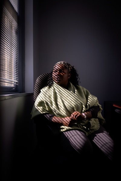 A young Black woman poses for a portrait while wearing a green shawl and a colorful headband.