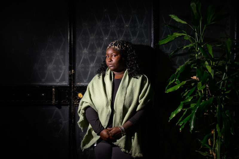 A young Black woman poses for a portrait while wearing a green shawl and a colorful headband.