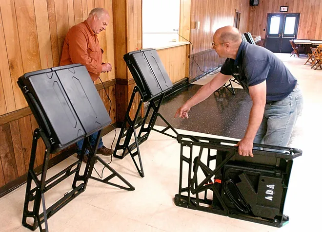 Rapid Transit Inc. owner and president Bob Mang, left, and employee Jerry Fellows, right, place new voting machines inside Belle Valley Fire Hall on May 15, 2006, in preparation for Tuesday's election. Fellows holds a machine that uses voice commands for people with impared sight.