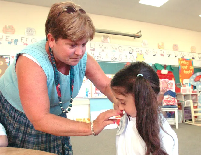 Our Lady of Peace kindergarten teacher Mary Zebrowski pins a name tag on Jasmine Meola, 5, in August 2007.