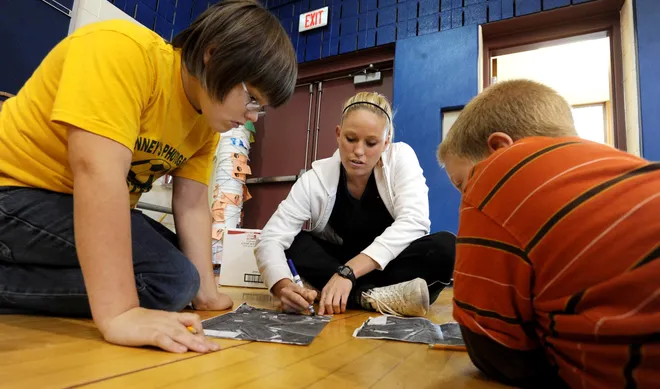 Wattsburg Elementary School physical education and health teacher Bethany Lawrence, center, goes over map routes with fourth-grade students Richard Beeman, left, and Michael Keener in the school gymnasium during an orienteering lesson Oct. 14, 2009.