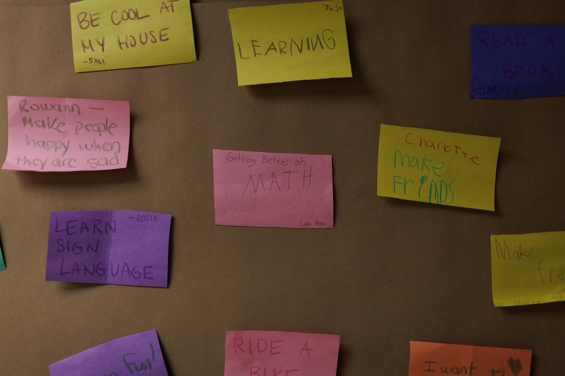 A bulletin board covered in colorful sticky notes with handwritten goals and messages from children.