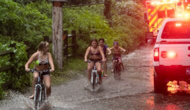 Cyclists navigate Isaias-related floodwaters along the Schuylkill in 2020 as Philadelphia fire and police respond to an incident nearby.