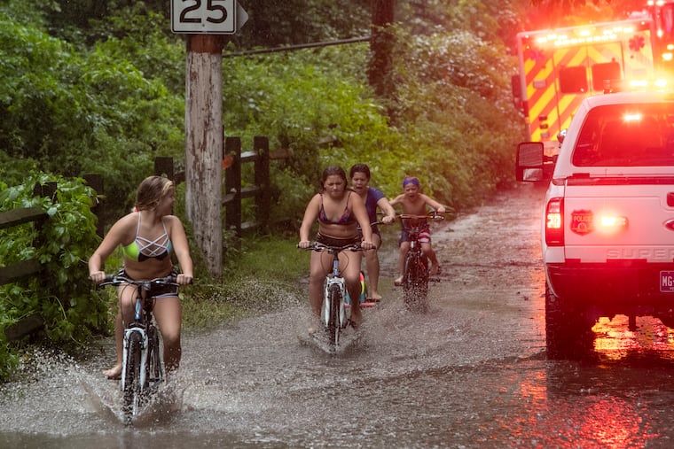 Cyclists navigate Isaias-related floodwaters along the Schuylkill in 2020 as Philadelphia fire and police respond to an incident nearby.