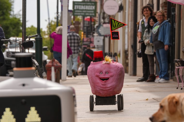 Orifice the Awebot trails an Uber Eats robot on the streets of Old City as a confused yellow Labrador retriever looks on.