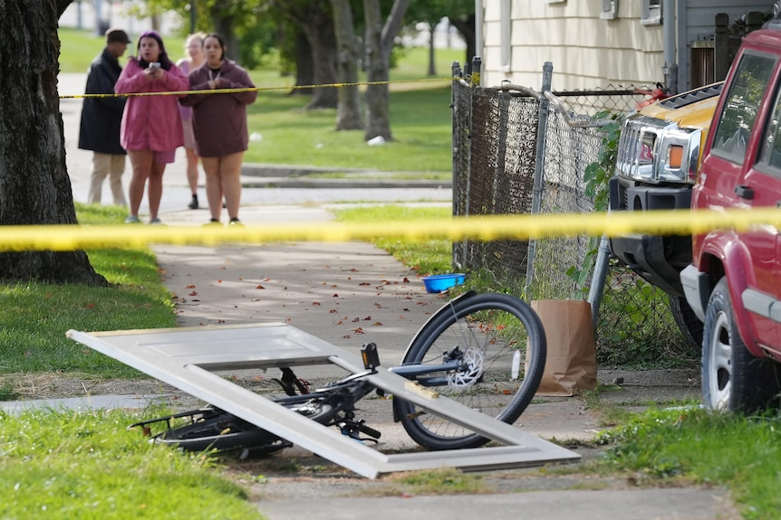 Four people stand behind yellow police tape.