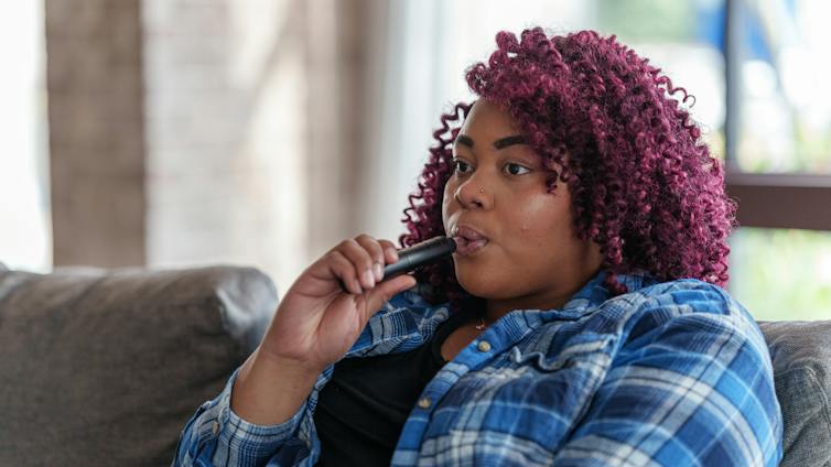 Woman sits on couch and vapes
