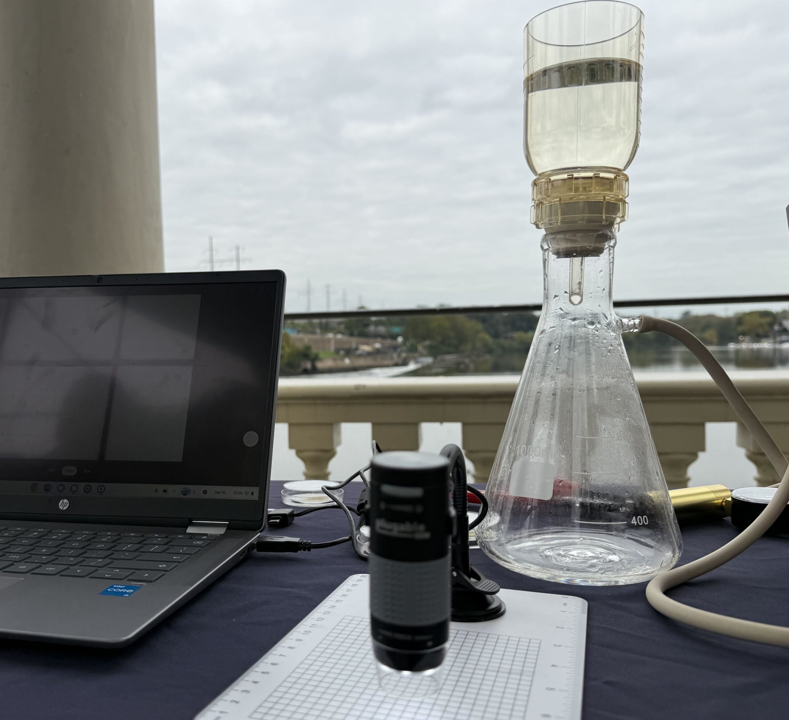 A laptop computer sits on a desk next to lab equipment used to identify microplastics in water.