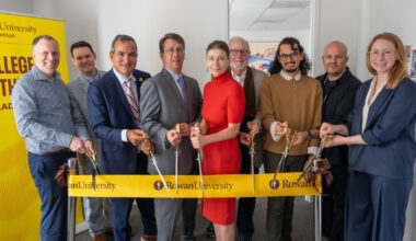Rowan University leadership, faculty and students stand shoulder to shoulder. Several people hold large scissors as they prepare to cut a ribbon that reads: Rowan University.