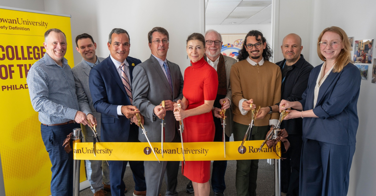 Rowan University leadership, faculty and students stand shoulder to shoulder. Several people hold large scissors as they prepare to cut a ribbon that reads: Rowan University.