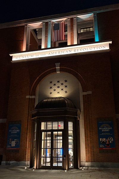 Museum of the American Revolution entrance illuminated at night with flag display.
