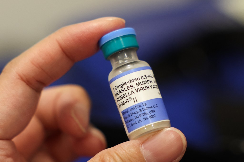 A hand holds a single-dose vial of the Measles, Mumps, and Rubella (MMR) vaccine.