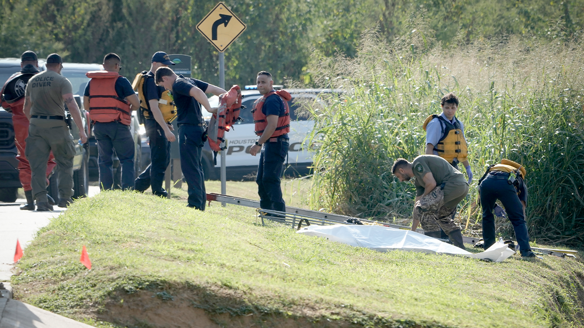 First responders wearing PFDs place a sheet over a body recovered from a bayou in Houston