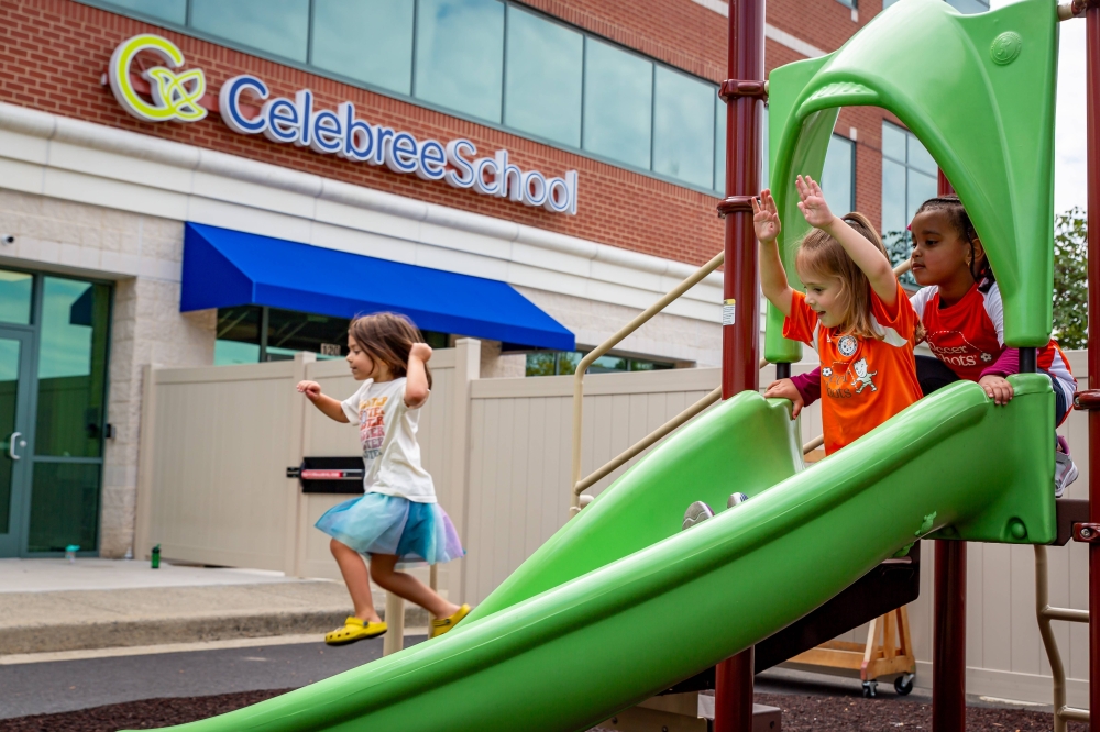 Children playing on a green slide in front of a building featuring Celebree School signage.