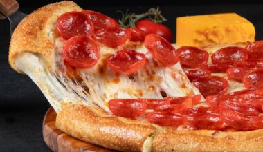 A slice of pepperoni pizza being pulled away from a pizza pie while cheese strings stay connected to both enitites.