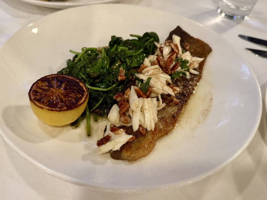 A plate for rainbow trout topped with crab, served with a side of lemon.