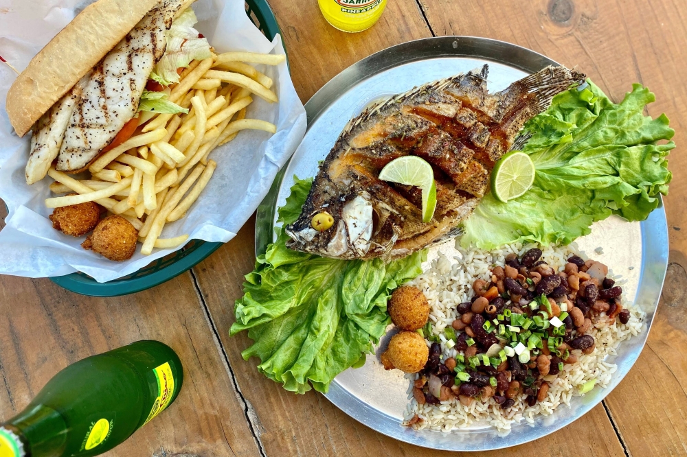 Overview of entire fish grilled on a plate and a fish sandwich.