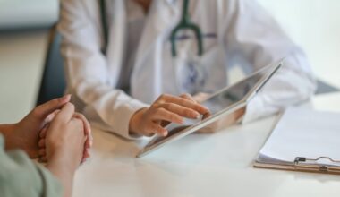 Person wearing a white medical coat and stethoscope points to a chart that another person's hands are next to.