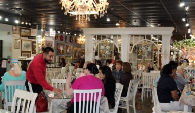Male standing next to a table with two seated females in a busy restaurant.