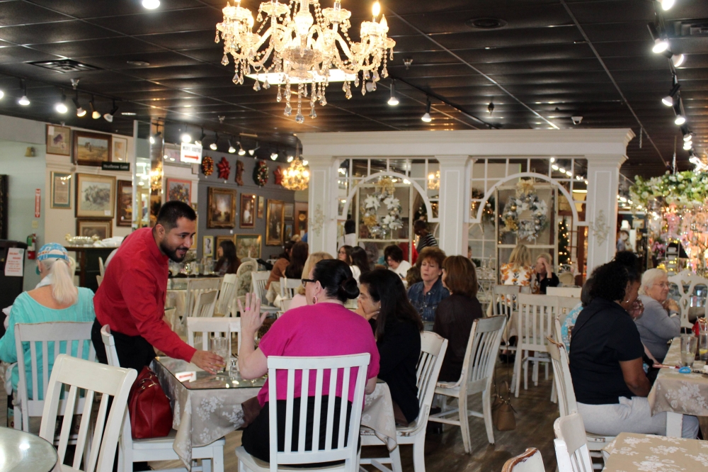 Male standing next to a table with two seated females in a busy restaurant.