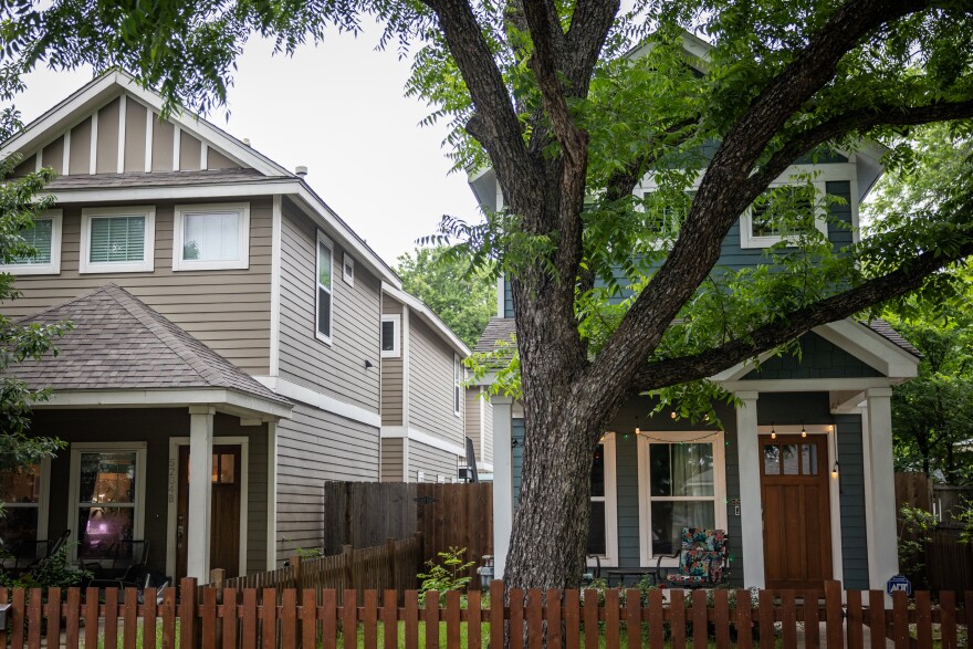 A two-story grey house next two a two-story blue house with a large tree in front of it.