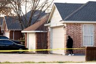 A woman peers around the corner at Grand Prairie police crime scene investigators working at...
