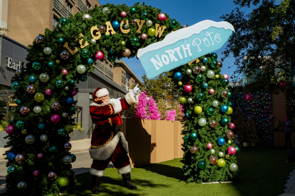 Santa Claus pointing at a North Pole sign