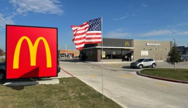 Exterior of a freestanding McDonald's eatery featuring a monument sign with the M yellow logo on red background and flag on a pole beside the monument sign.