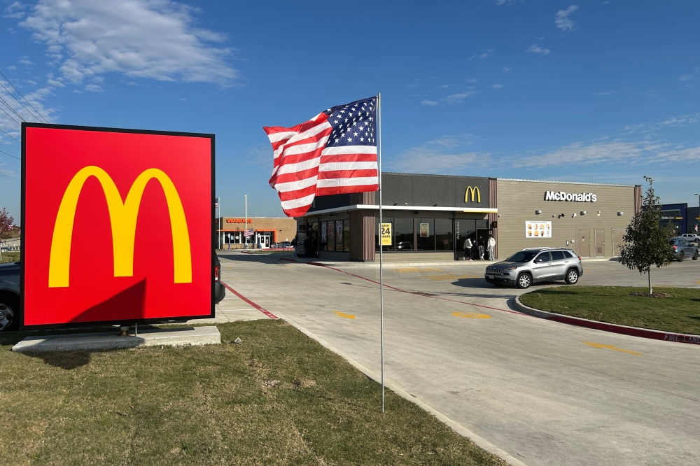 Exterior of a freestanding McDonald's eatery featuring a monument sign with the M yellow logo on red background and flag on a pole beside the monument sign.