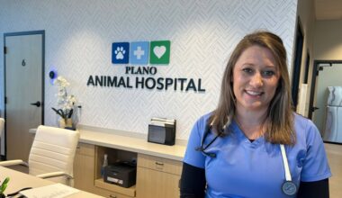Female wearing medical scrubs and a stethoscope around her neck stands in front of a wall featuring a Plano Animal Hospital sign.