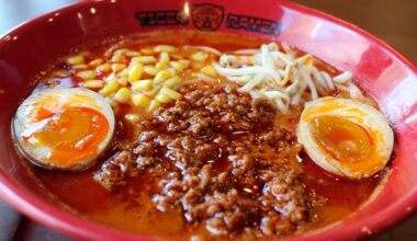 Red bowl featuring Tiger Ramen branding is filled with ramen, meat, eggs, corn and broth.