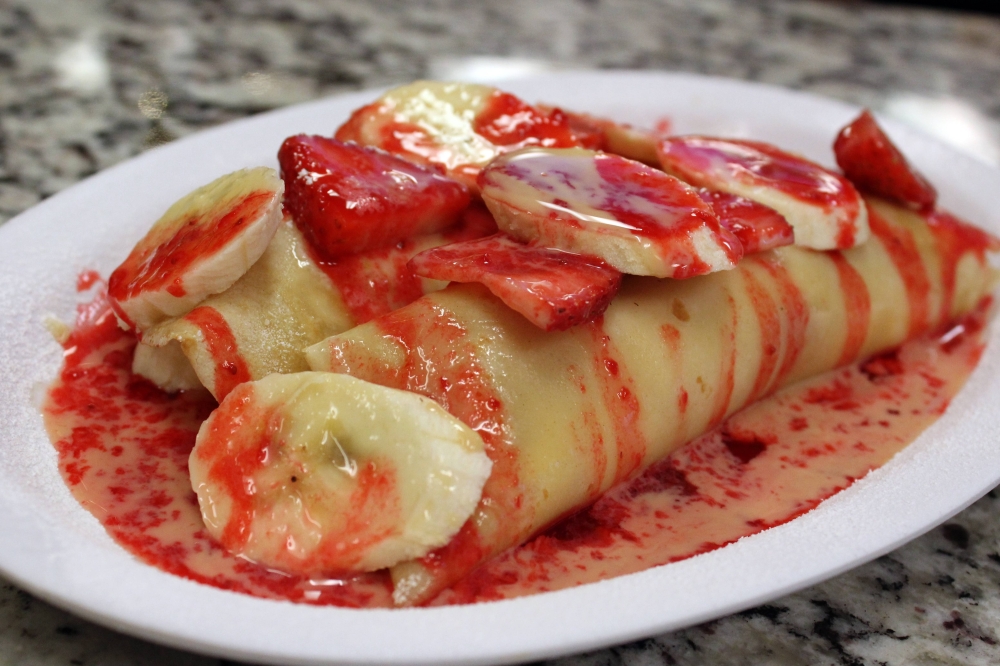 Crepes covered with bananas and a red sauce on a plate.