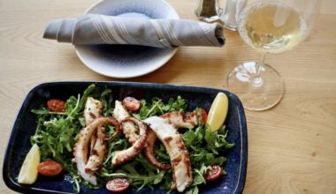 a plate with grilled octopus pizzas next to a wine glass