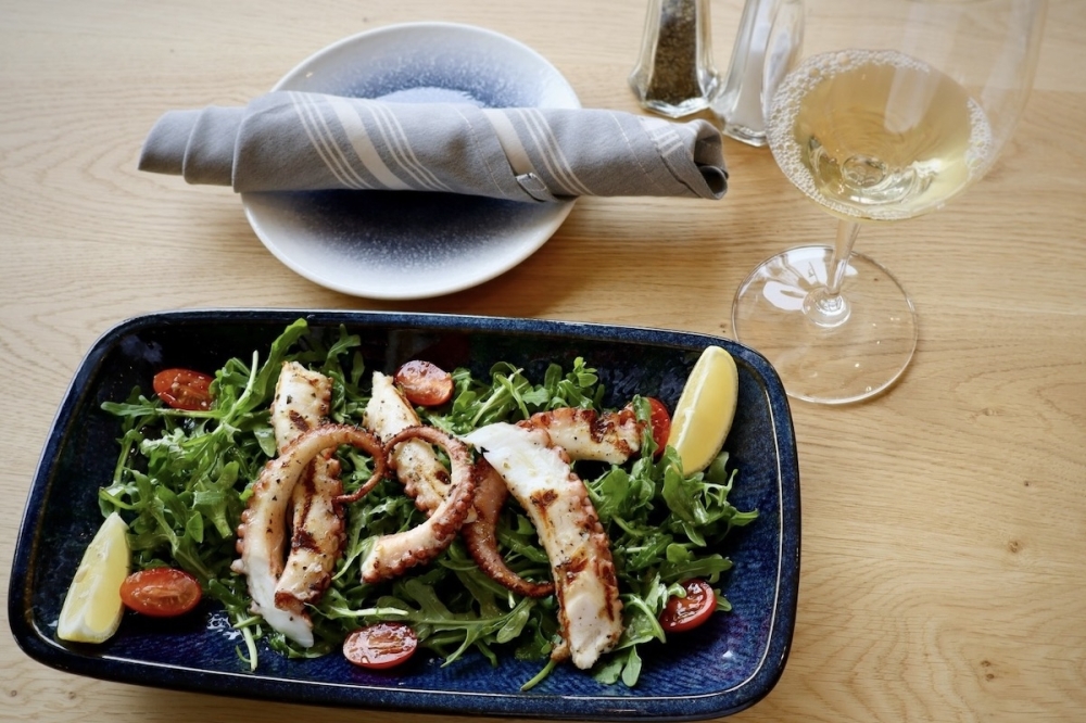 a plate with grilled octopus pizzas next to a wine glass