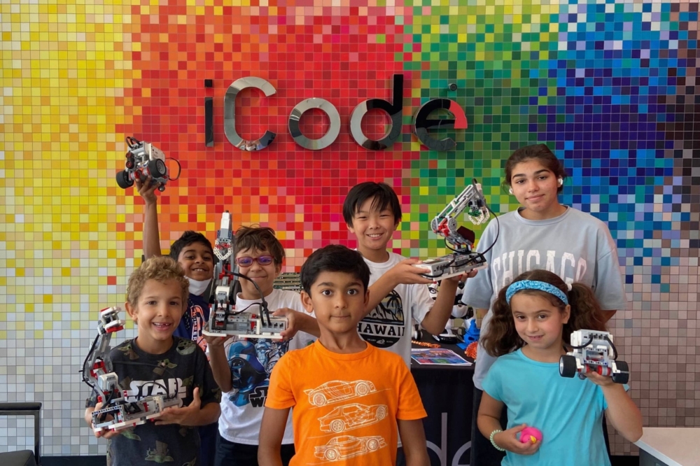 Group of children in standing in front of a brightly painted wall featuring iCode branding.