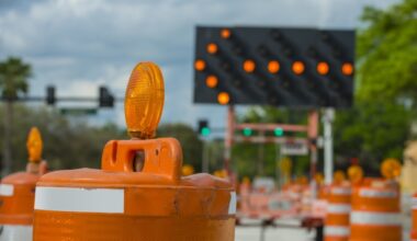 Orange and white traffic drums surrounding a sign redirecting traffic