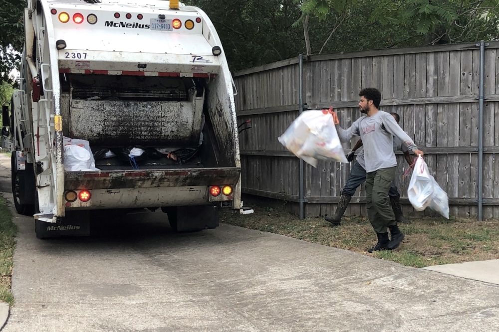 A man throwing two trash bags into the back of a garbage truck