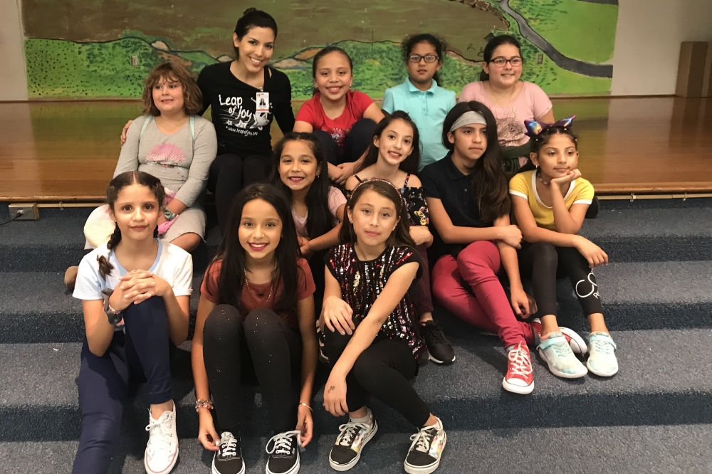 Monica Chin smiles for a photo with a group of young female dance students