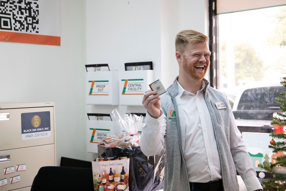 A man in a printing shop smiling and holding a business card