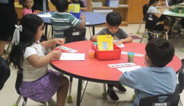 Elementary students sit around a table and work on school work