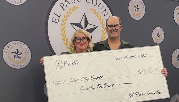 A couple wearing eccentric glasses hold a big check made out to Sun City Super from El Paso County.