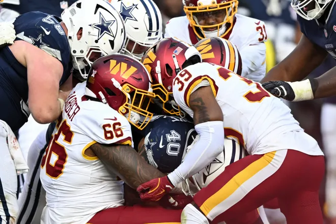 LANDOVER, MARYLAND - DECEMBER 25: Ricky Barber #66 and Jeremy Reaves #39 of the Washington Commanders tackle Hunter Luepke #40 of the Dallas Cowboys in the third quarter of a game at Northwest Stadium on December 25, 2025 in Landover, Maryland. (Photo by Greg Fiume/Getty Images)
