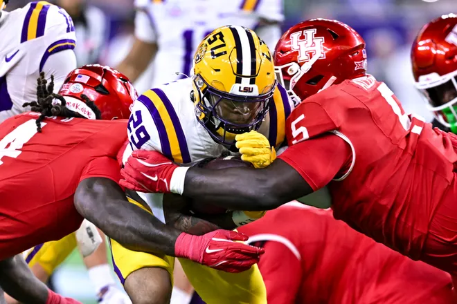 Dec 27, 2025; Houston, TX, USA; Louisiana State Tigers running back Caden Durham (29) runs the ball as Houston Cougars defensive end Brandon Mack (4) and defensive lineman Carlos Allen (5) attempt to tackle during the first half at NRG Stadium. Mandatory Credit: Maria Lysaker-Imagn Images
